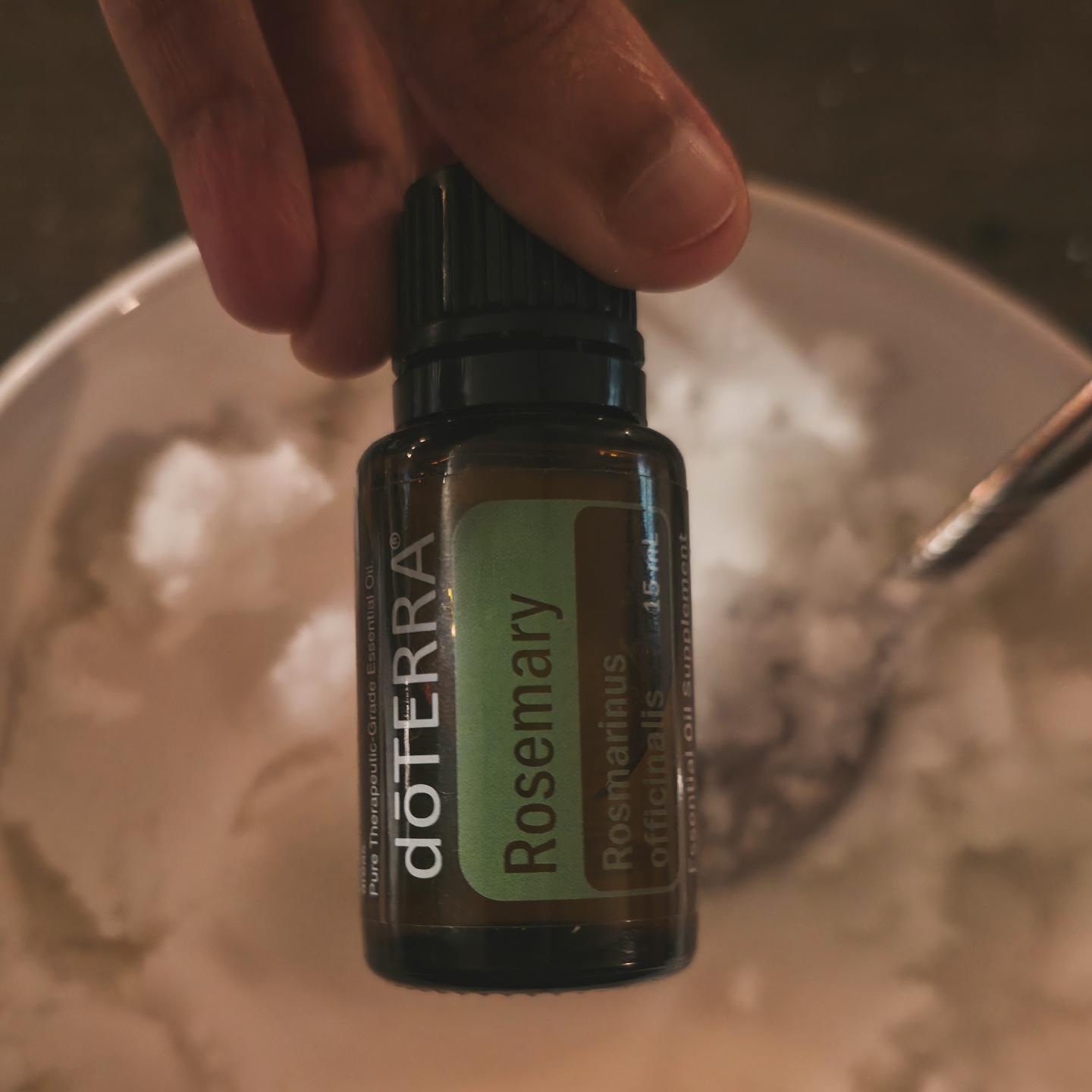 Bottle of rosemary essential oil held above a mixing bowl